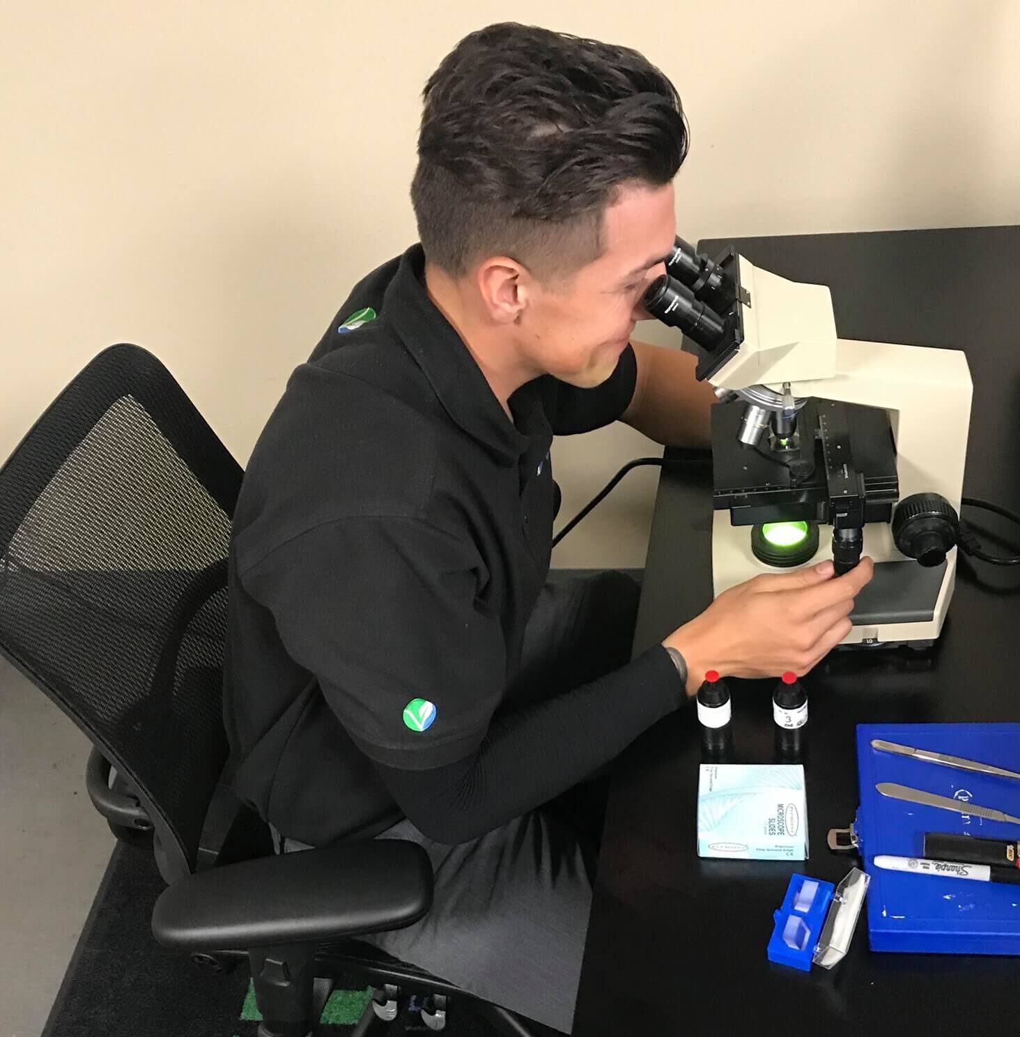 A Vert Environmental specialist in a branded polo shirt conducting detailed microscopic analysis of environmental samples in a laboratory setting.
