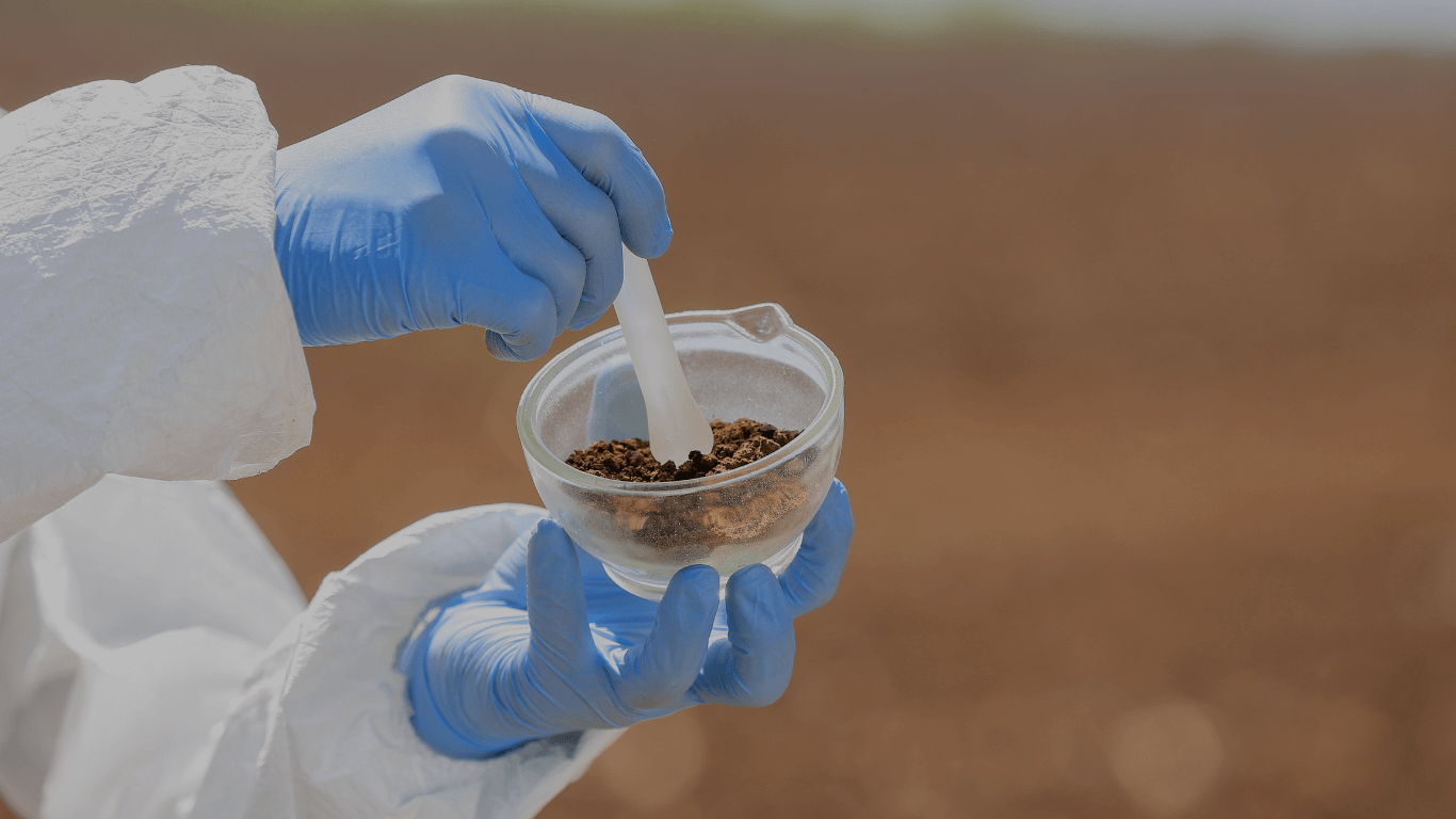 Environmental water quality analysis: A close-up of a glass vial sample held by a technician during field testing in a natural outdoor setting.