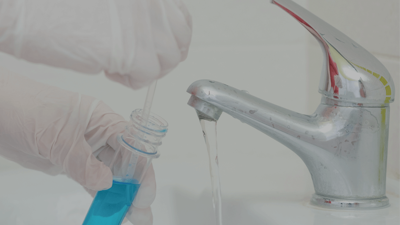 Professional water quality testing: A technician in white gloves uses a pipette to collect a sample from a running tap into a laboratory test tube with blue liquid.